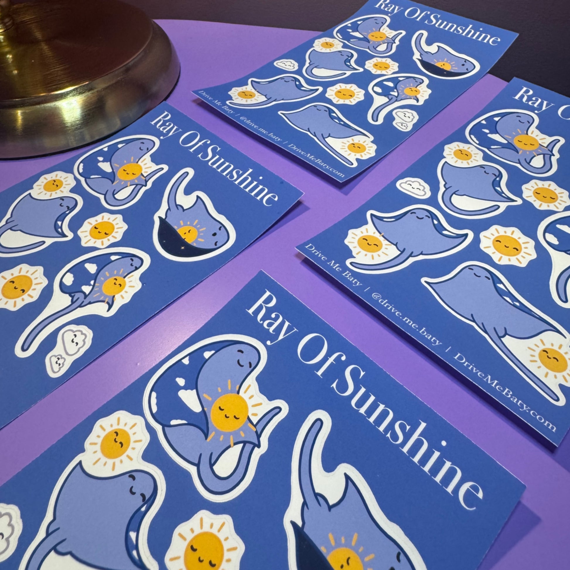 Sticker sheets with 'Ray Of Sunshine' design on a purple surface