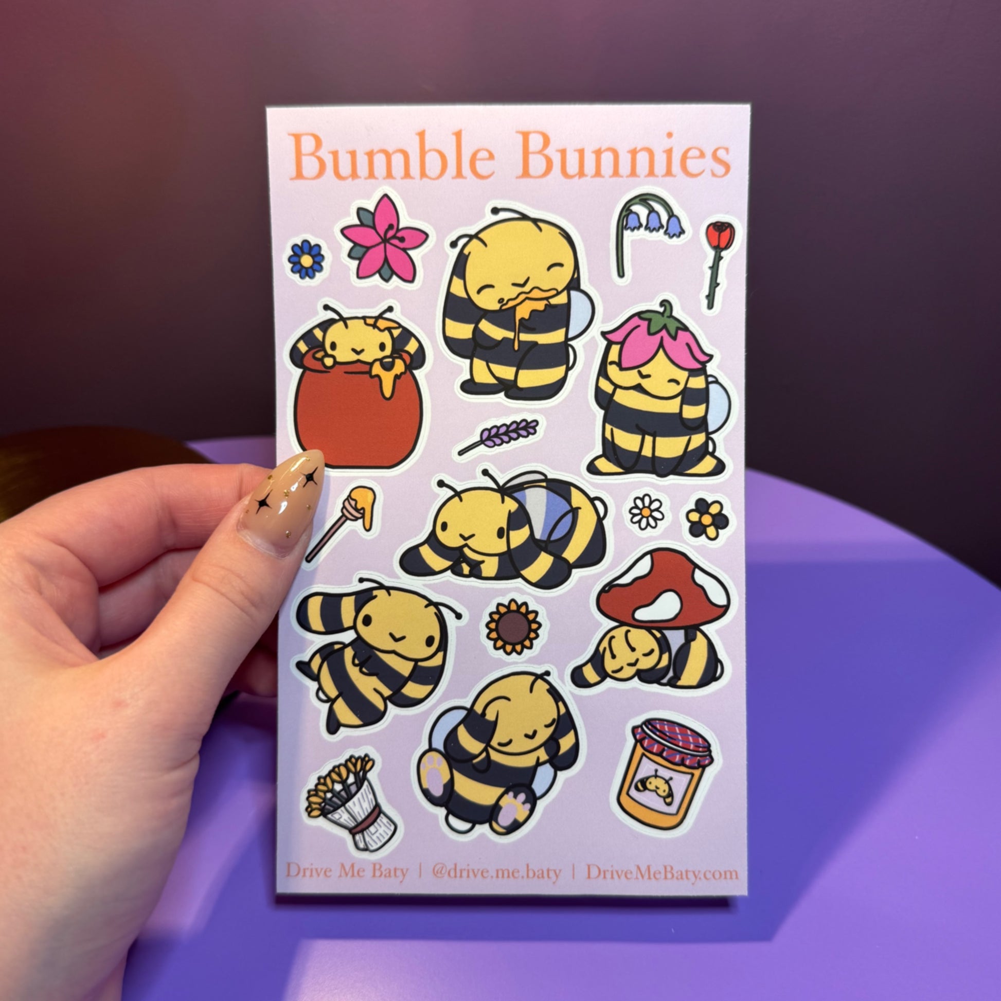 Pack of 'Bumble Bunnies' stickers held by a hand on a purple surface.