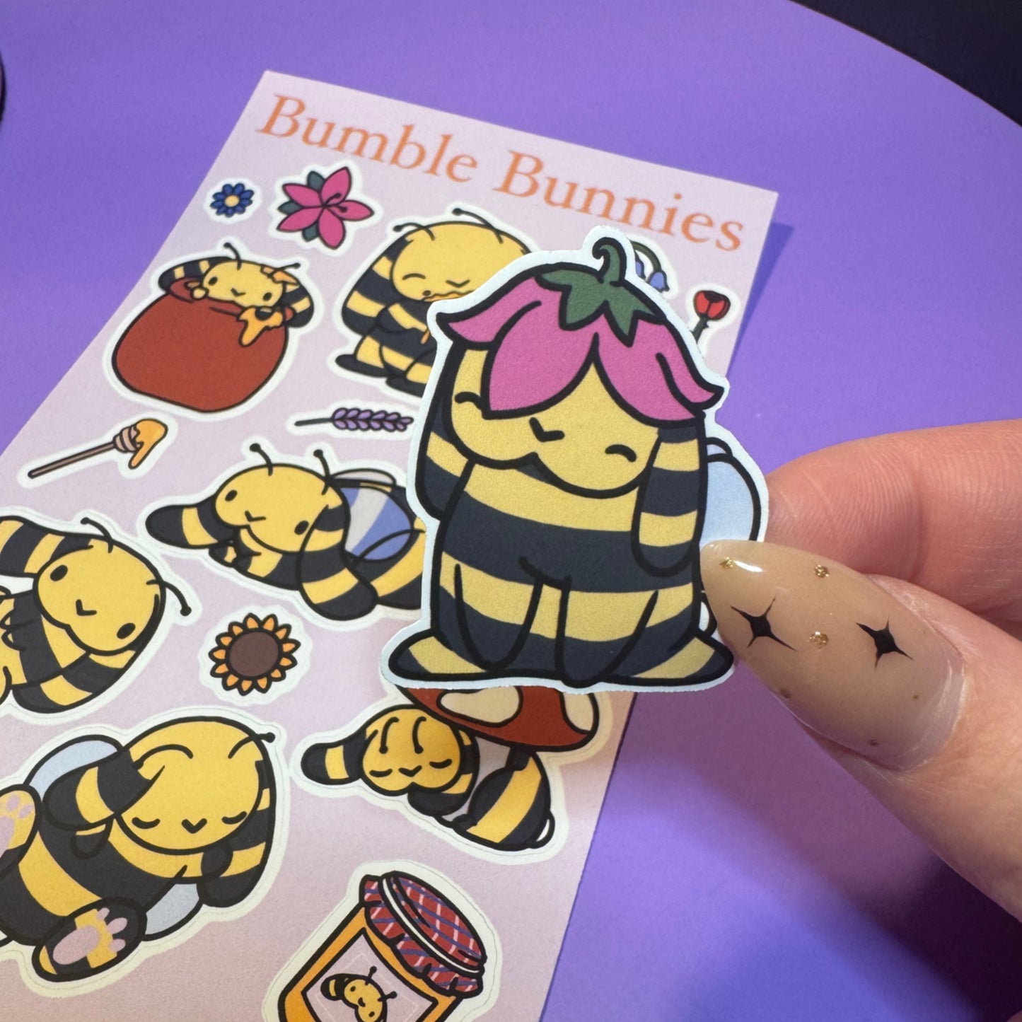 Sheet of 'Bumble Bunnies' stickers with a hand holding one sticker against a purple background.