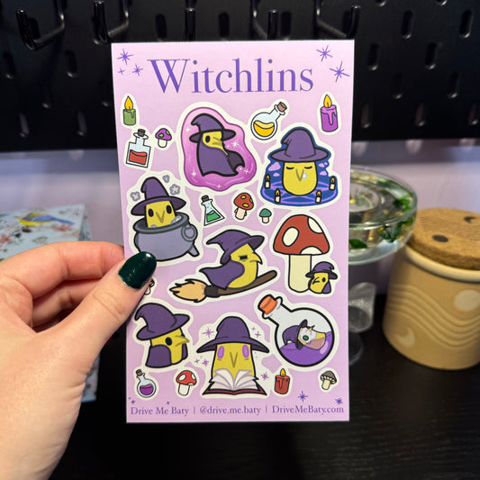 A Witchlin sticker sheets, including a collection of small green rectangles with pointy noses, black beady eyes and adorned in a purple witches hat and cape.
The Witchlins are doing lots of different things including; riding a broom, sitting in a cauldron, hiking under a mushroom, swimming in a potion bottles, reading spells, standing up and casting spells.